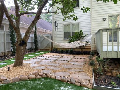 Backyard patio with stone pavers, hammock, tree, and white house siding