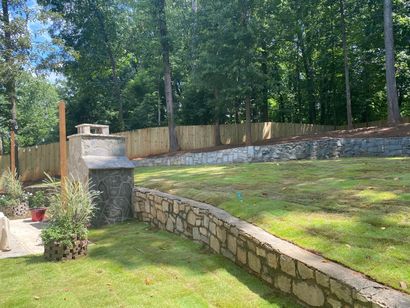 Stone retaining wall along a grassy backyard with trees and a wooden fence in the background
