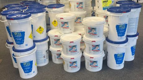 A bunch of white buckets with blue lids are stacked on top of each other.