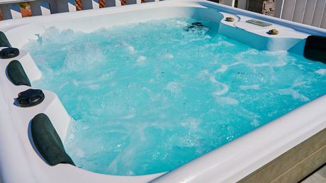 A white hot tub filled with blue water on a deck