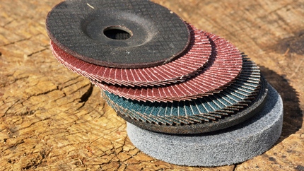 Assorted sanding and grinding discs in various colors, stacked on a wooden surface.