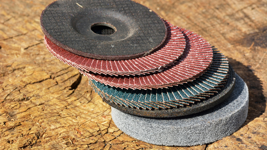 Stack of abrasive sanding discs in various colors on wooden surface.