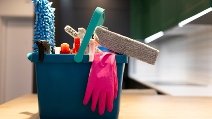 Blue cleaning bucket with gloves, sponge, and tools on a wooden surface, in a kitchen setting.