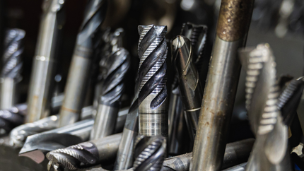 Close-up of a collection of metal drill bits, some with spiral cutting edges, in a workshop setting.