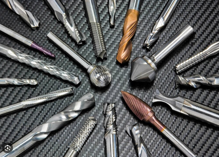 An assortment of shiny metal drill bits and milling tools arranged on a textured black surface.