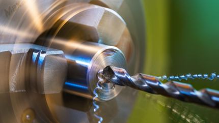 Drill bit creating a hole in rotating metal cylinder on a lathe.
