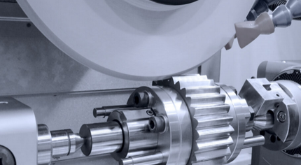 A gear being precisely ground by a rotating wheel in a metalworking machine.