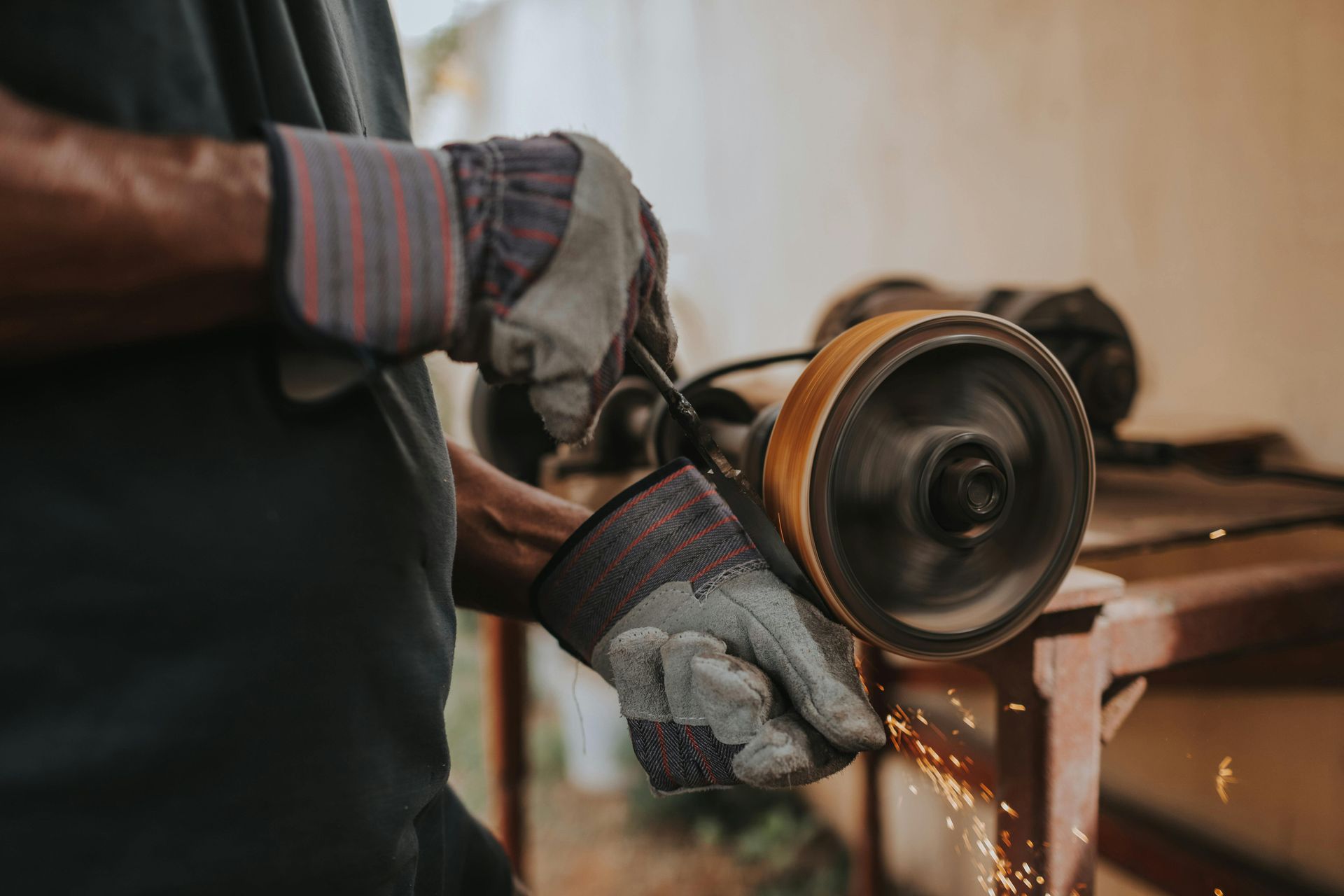 A person wearing work gloves grinding metal with a spinning wheel, creating sparks.