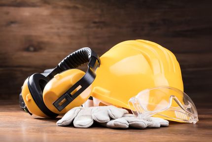 Yellow hard hat, ear muffs, gloves, and safety glasses on a wooden surface, safety equipment.