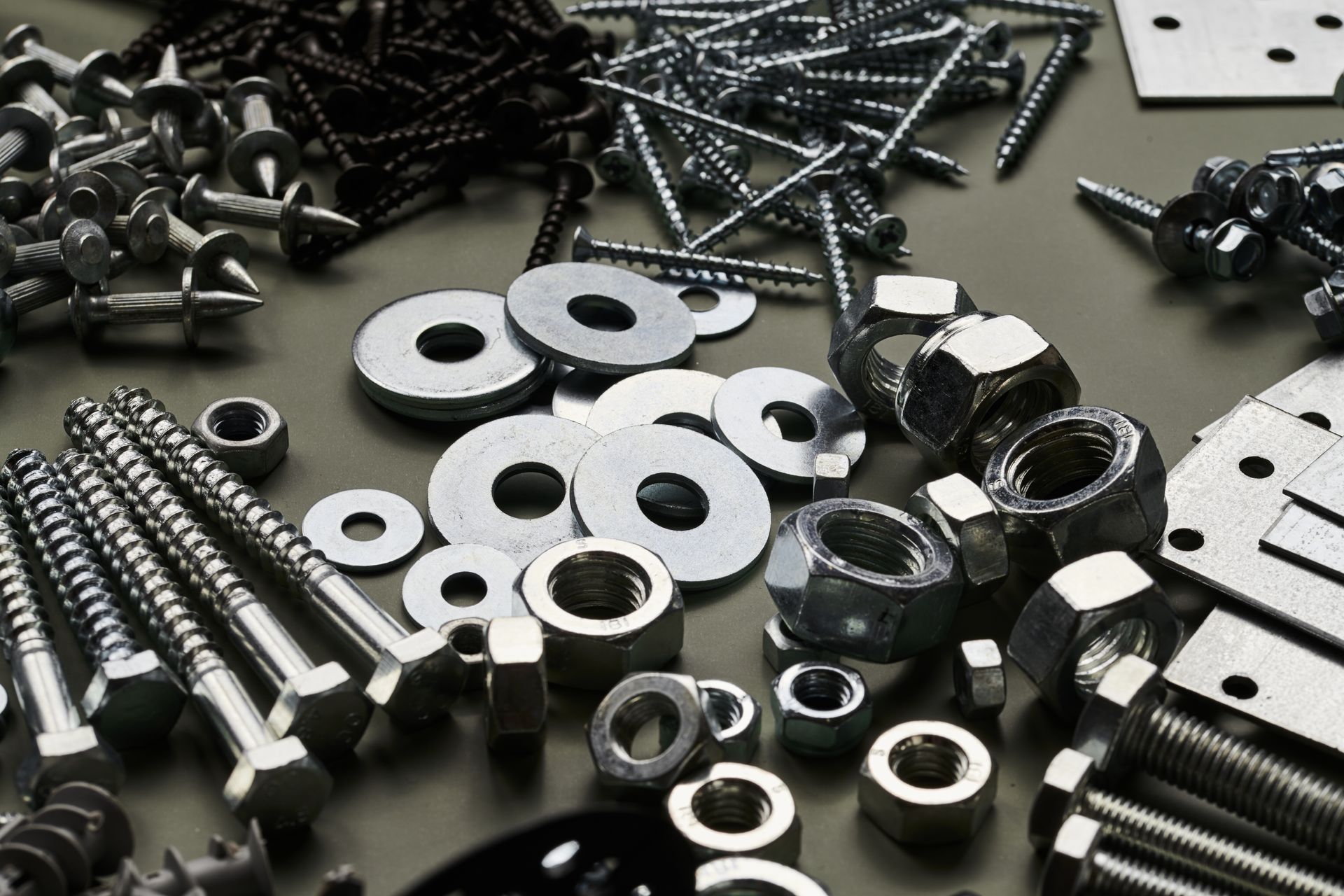 Assorted metal fasteners: screws, nuts, bolts, and washers, scattered on a surface.