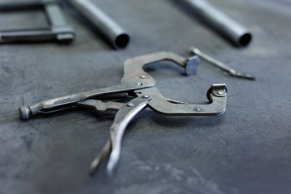 Metal locking pliers next to metal tubes on a dark surface.