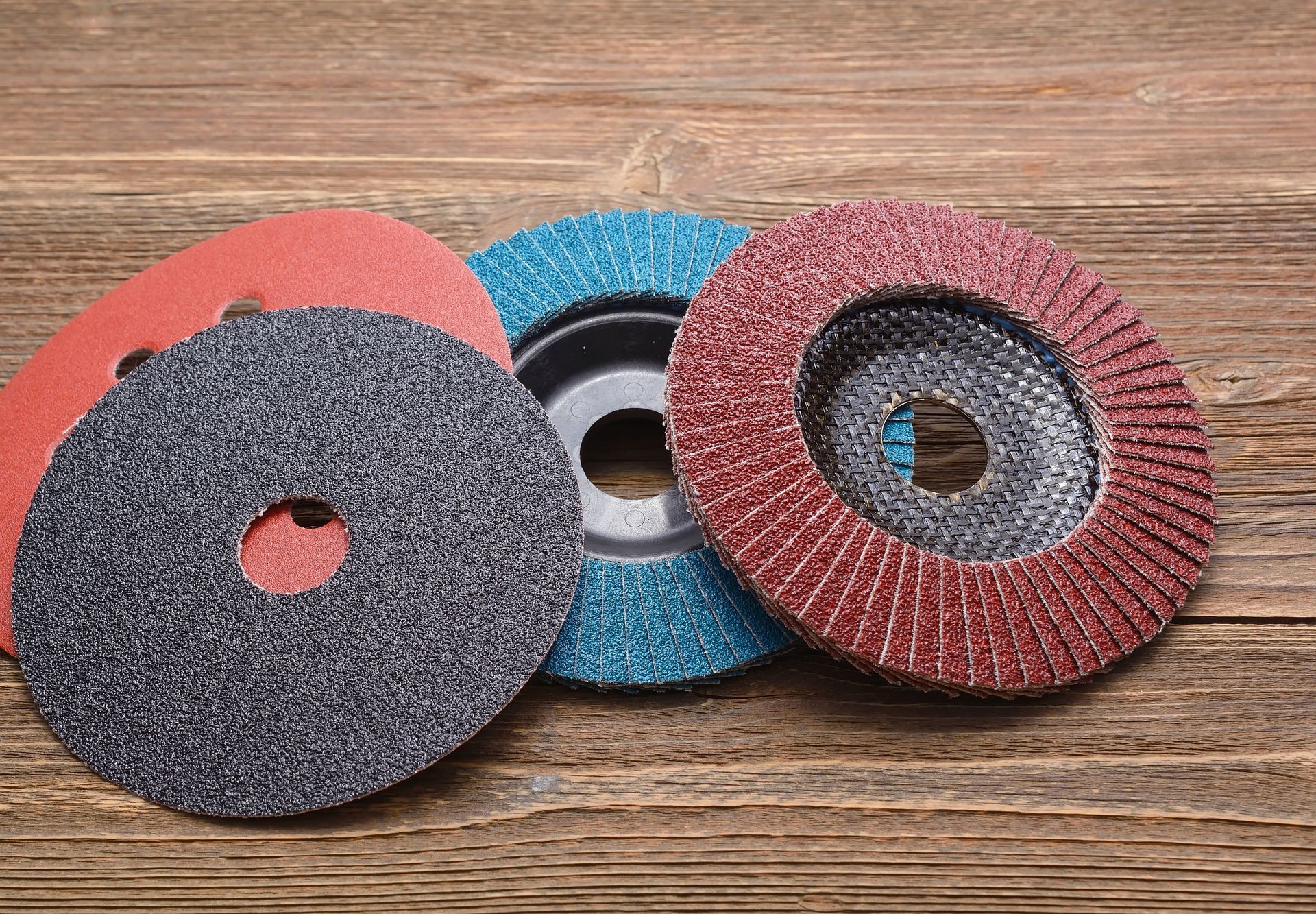 Various sanding discs on a wooden surface: red, blue, gray, and brown.