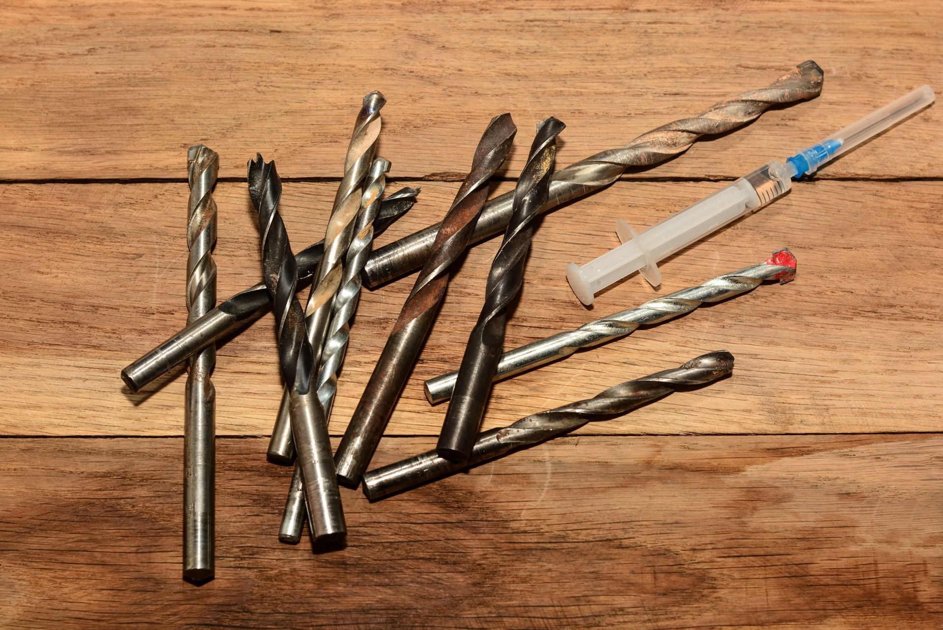 Drill bits and a syringe on a wooden surface.