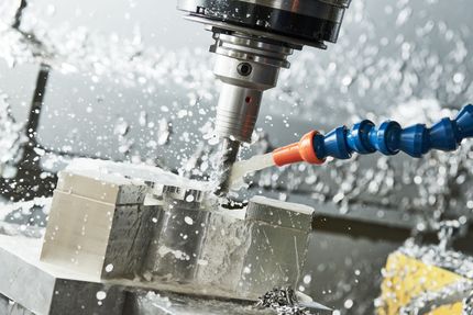 CNC machine cutting metal block with coolant spray.