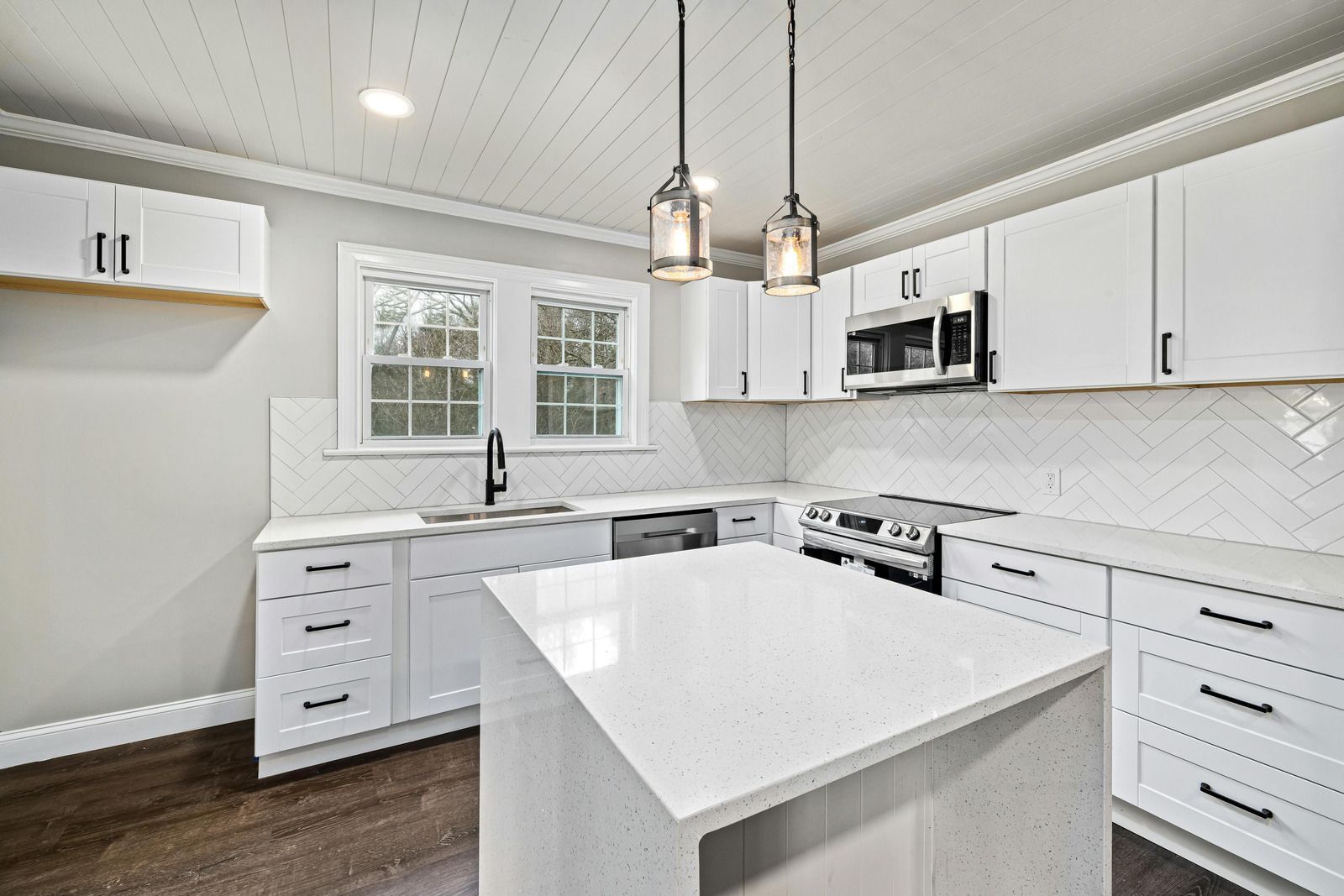Bright white modern kitchen with island, stainless appliances, pendant lights, and dark wood floor