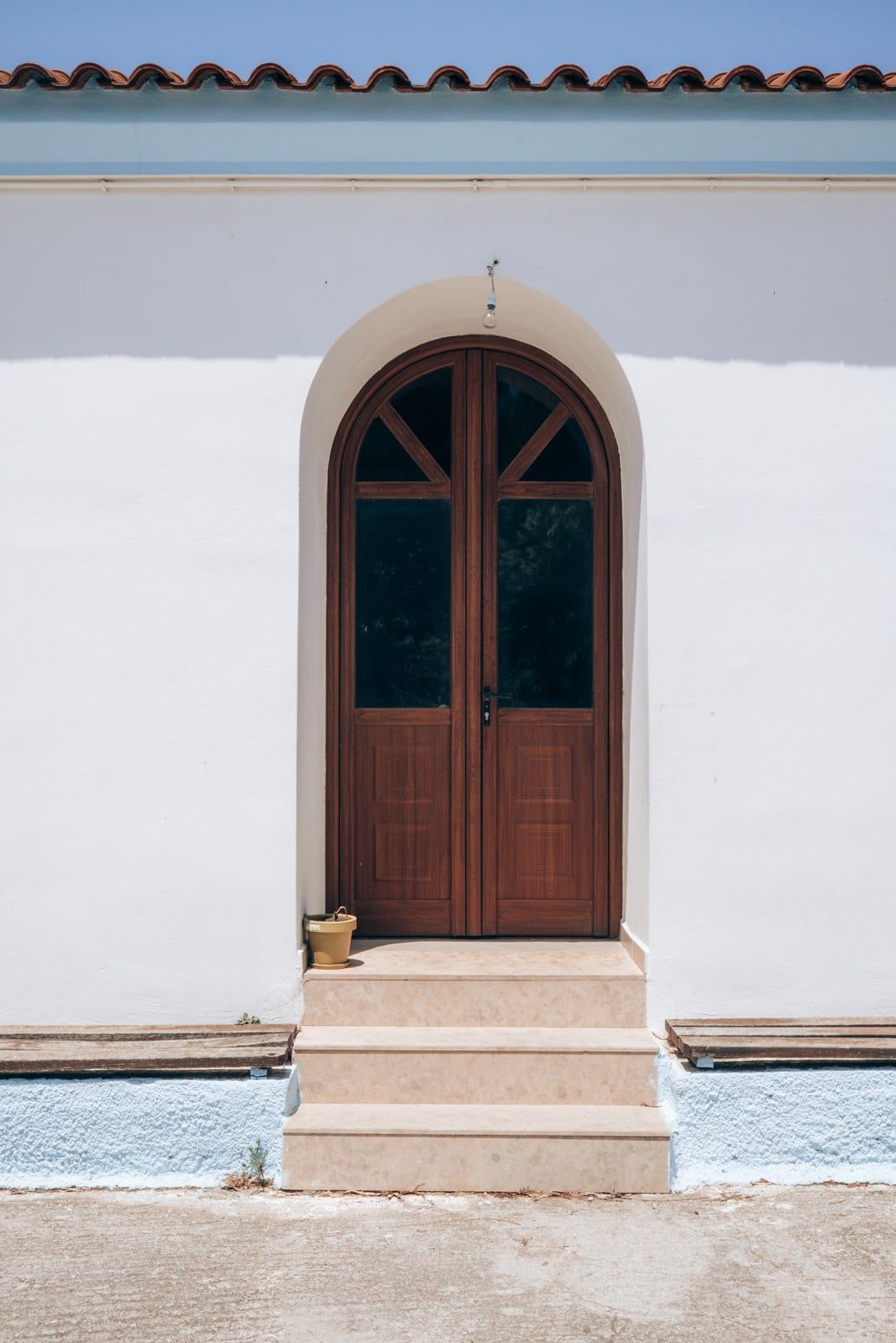 Arched wooden door centered in a white stucco wall with a small step and tiled roof edge