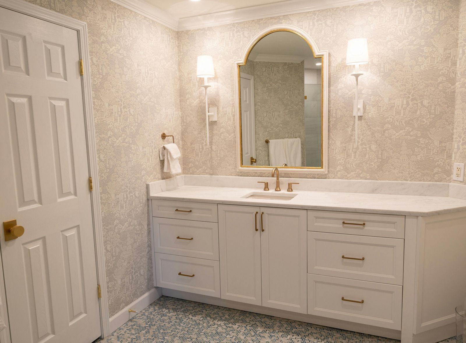 Bright white bathroom vanity with double sinks, gold hardware, and an arched mirror between wall sconces