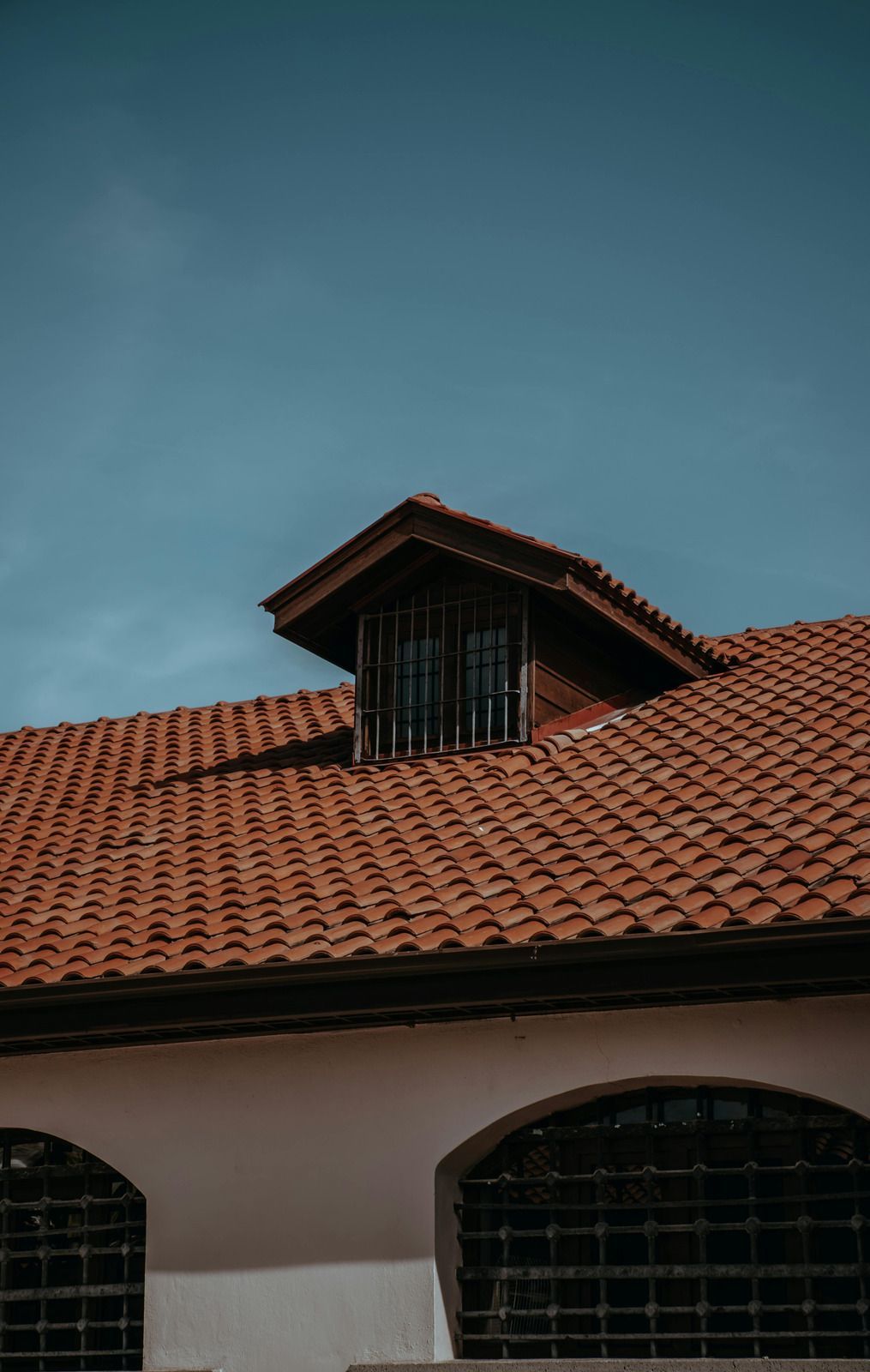 Red-tiled roof with a small dormer against a blue sky above arched windows