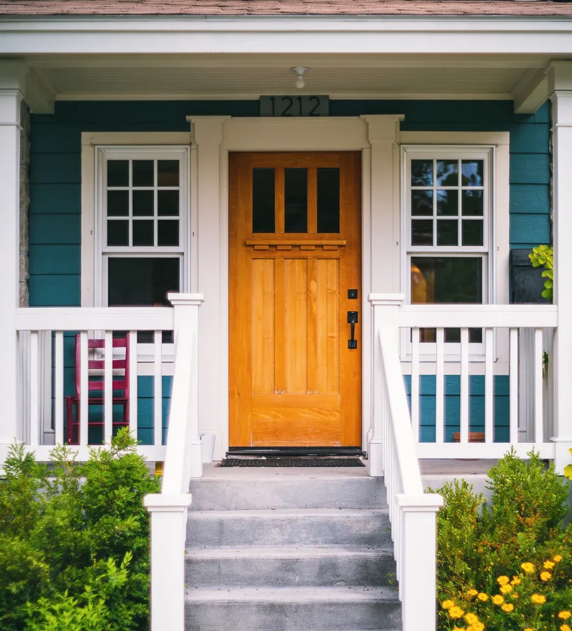 Front porch with orange door, white railings, teal siding, and steps leading up to the entrance