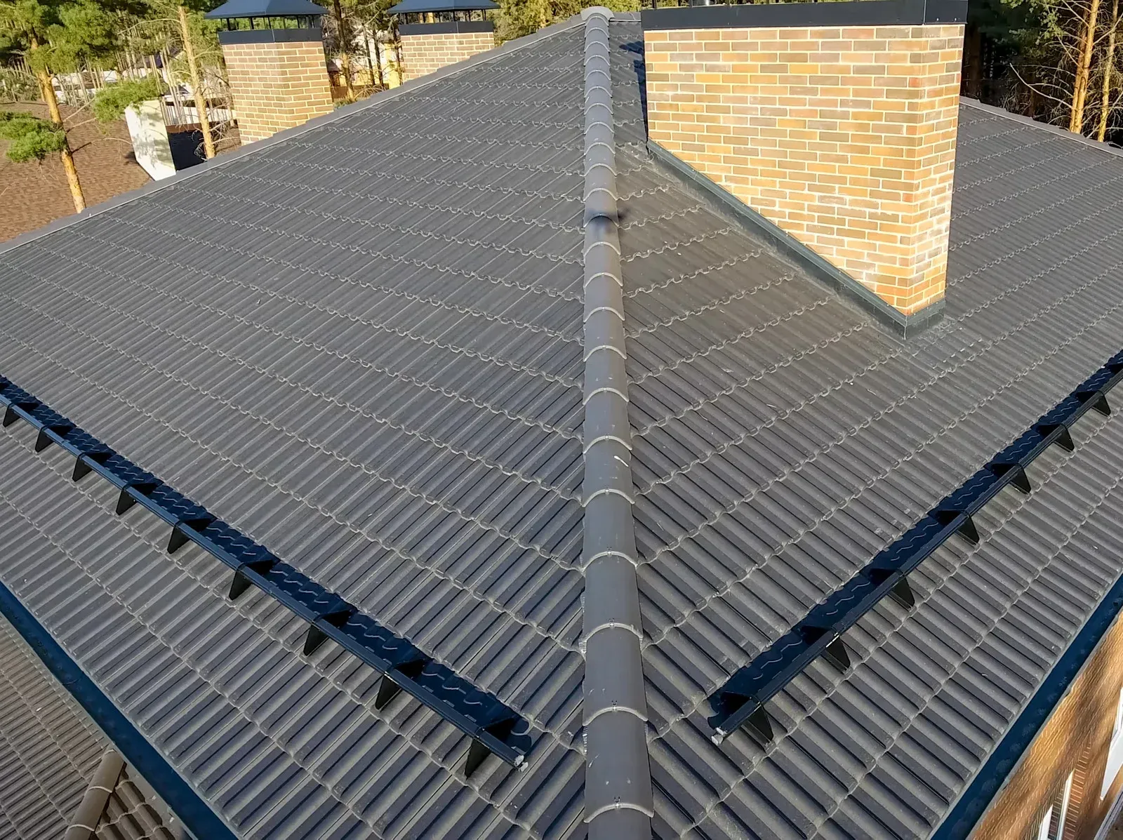 Roof with dark gray shingles and a central ridge, viewed from above beside a brick chimney.