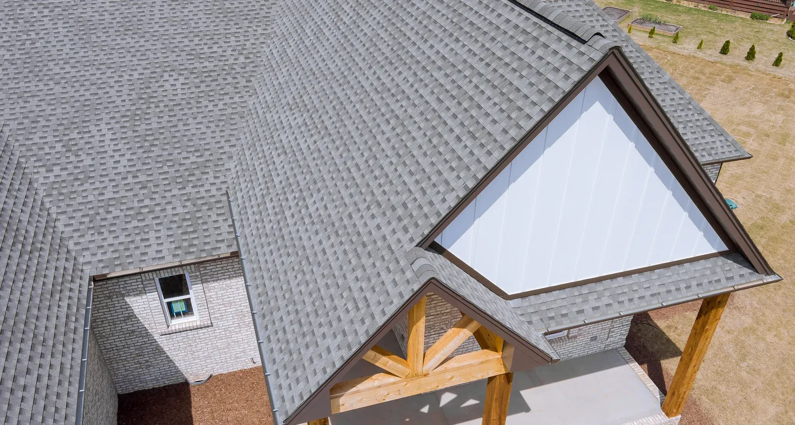 Aerial view of a gray-shingled house roof with a gable and porch beams.