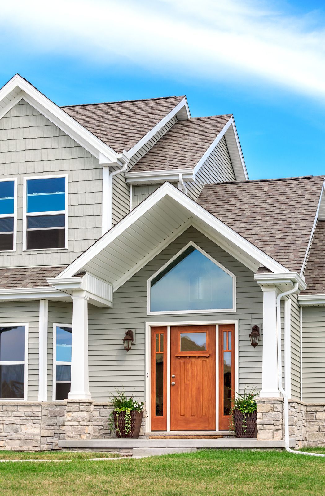 Modern gray house with stone accents, wood front door, and a gabled entry under a blue sky