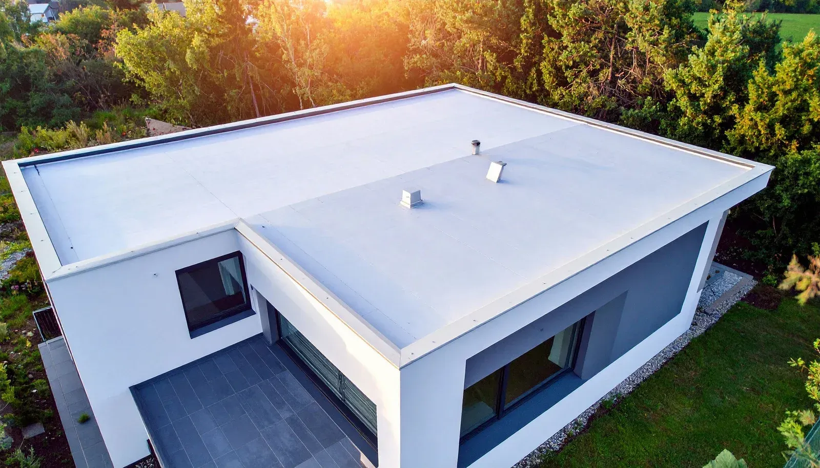 Modern white flat-roof house seen from above, surrounded by trees and greenery.