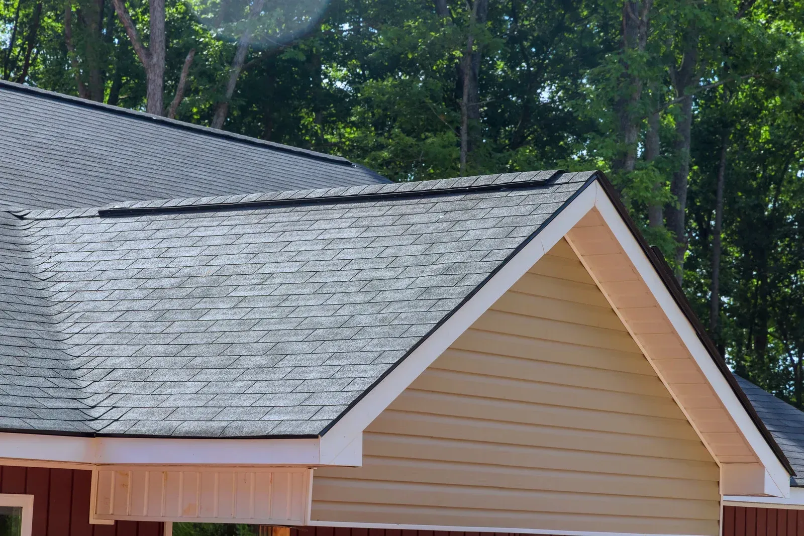 Gray shingled roof and beige house gable against tall green trees