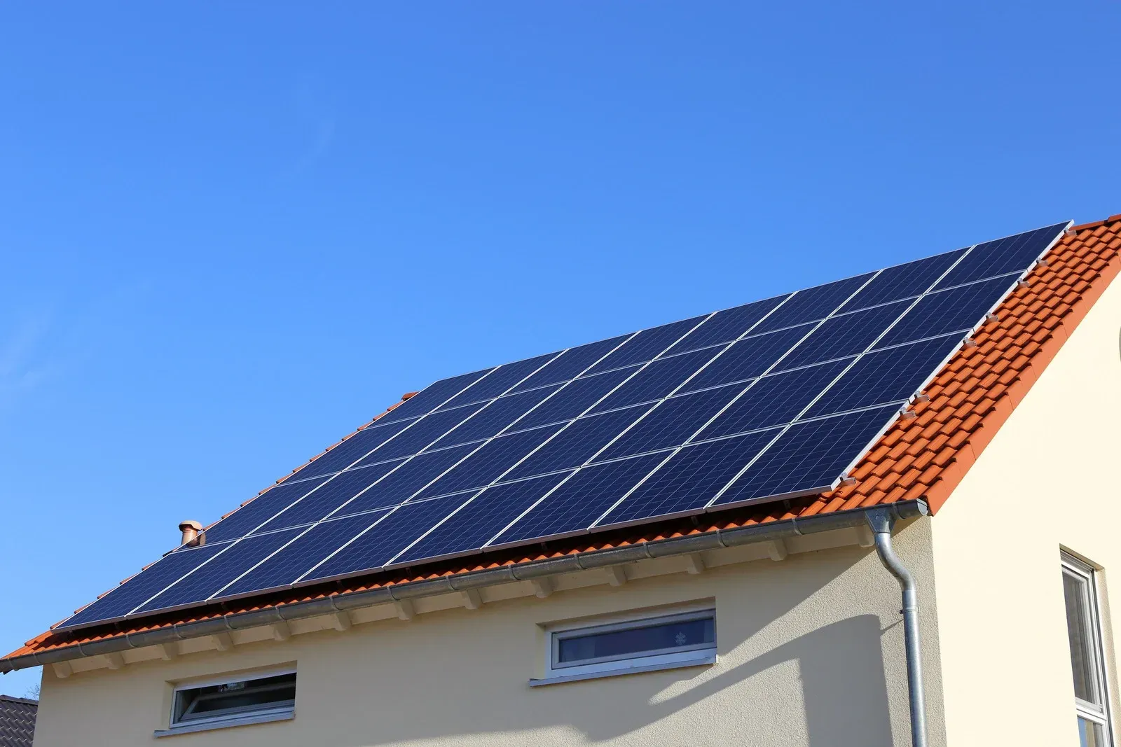 House roof with blue solar panels under a clear blue sky