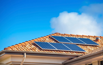 Solar panels mounted on a terracotta-tiled rooftop under a blue sky