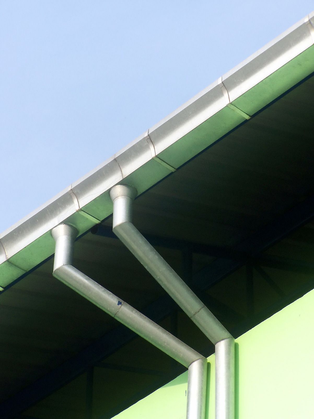 Close-up of green roof eaves with white gutter pipes against a blue sky