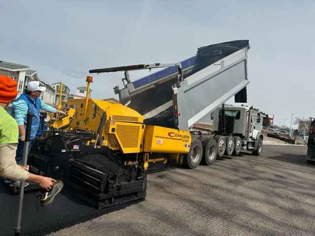 A dump truck is being loaded with asphalt on a construction site.