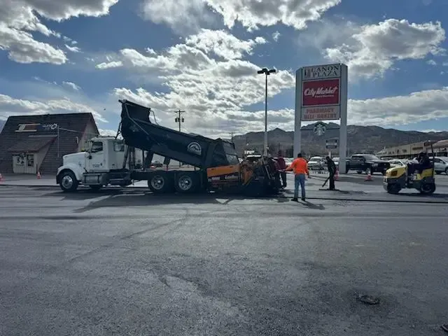 A dump truck is being loaded with asphalt in a parking lot.