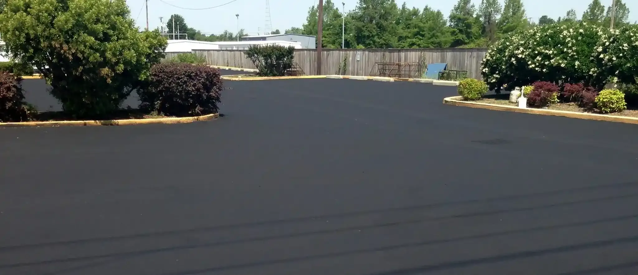 A black asphalt parking lot with trees and bushes in the background.