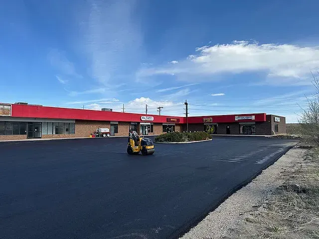 A forklift is driving down a paved driveway in front of a building.