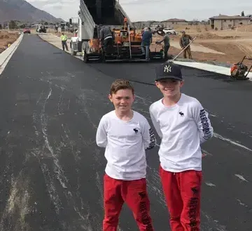 Two young boys are standing next to each other on a road.