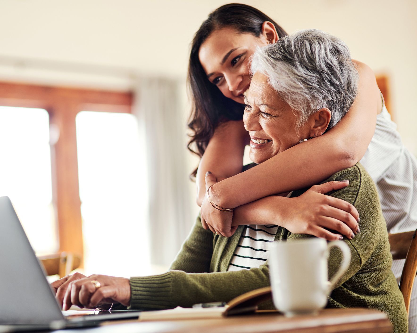 A young woman is hugging an older woman while using a laptop computer.