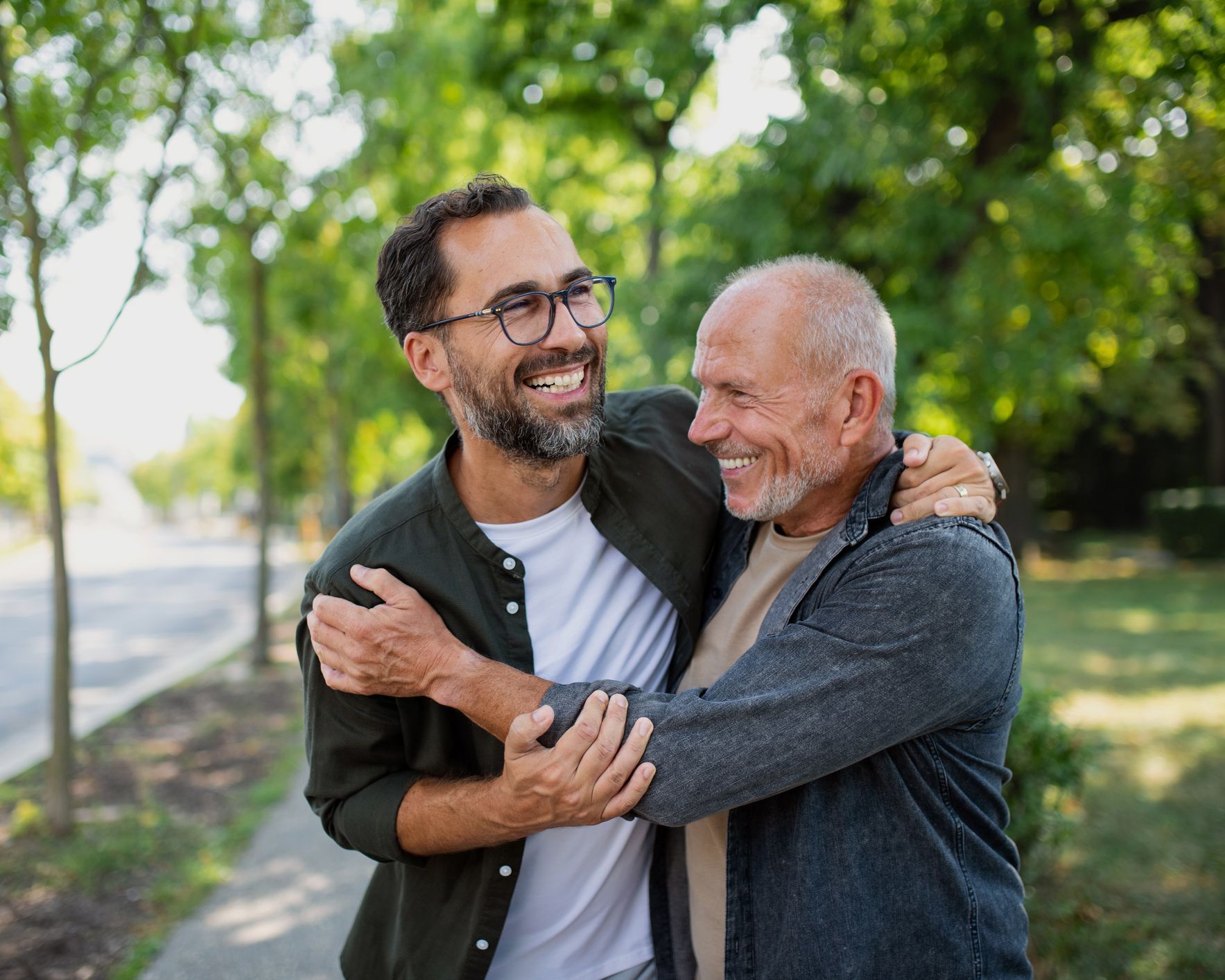 A young man is hugging an older man in a park.