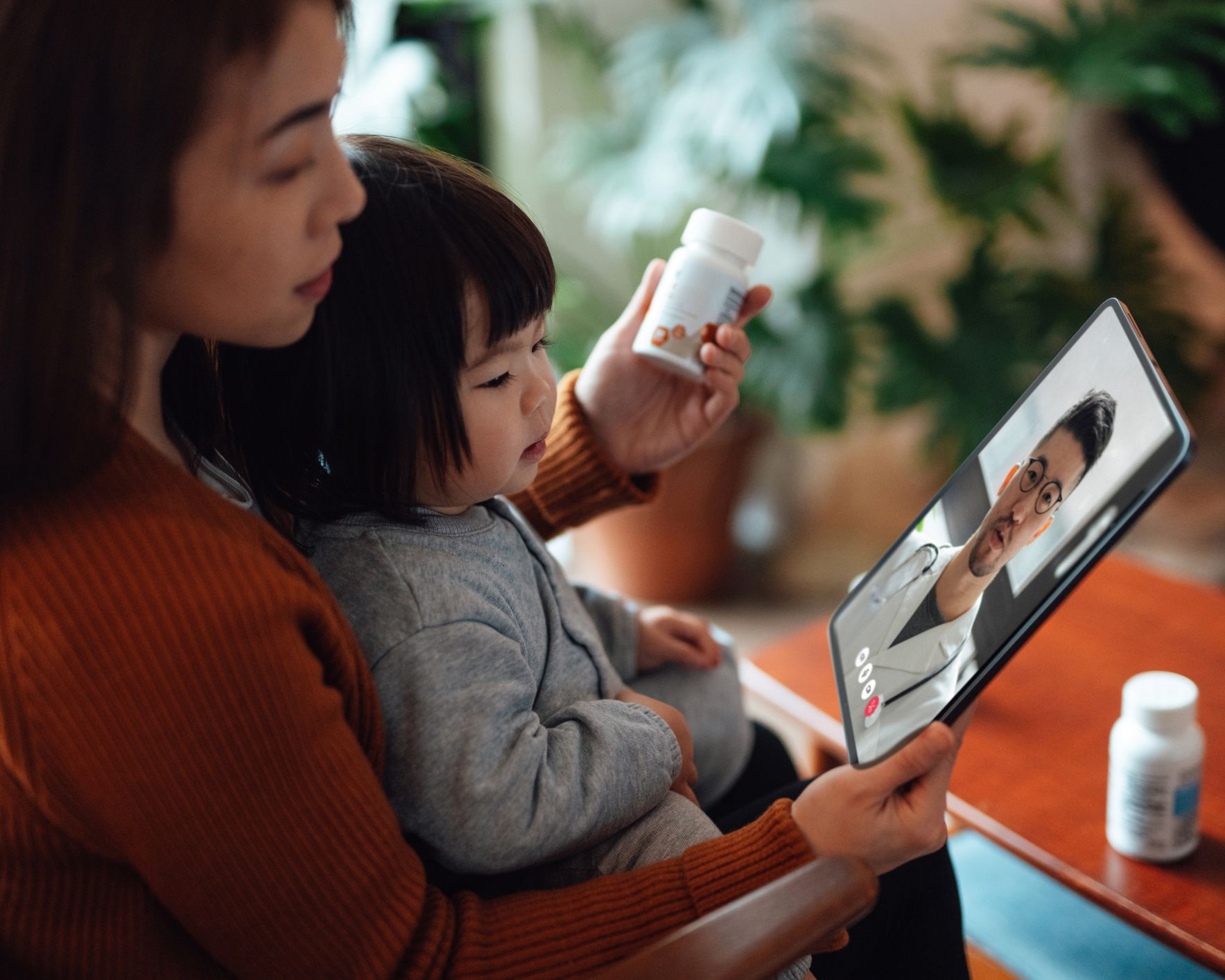 A woman is holding a child while looking at a tablet.