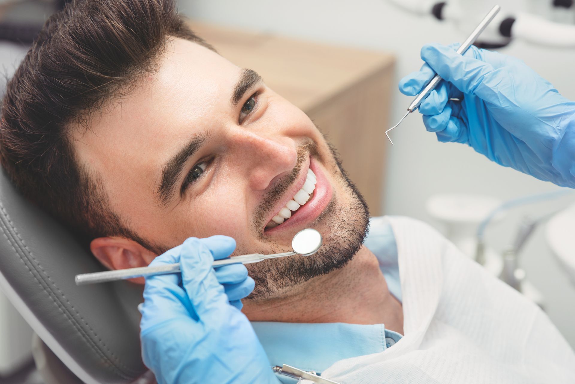 A man is sitting in a dental chair while a dentist examines his teeth.