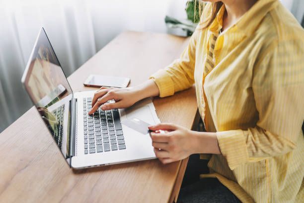 A woman is sitting at a desk using a laptop computer and holding a credit card.
