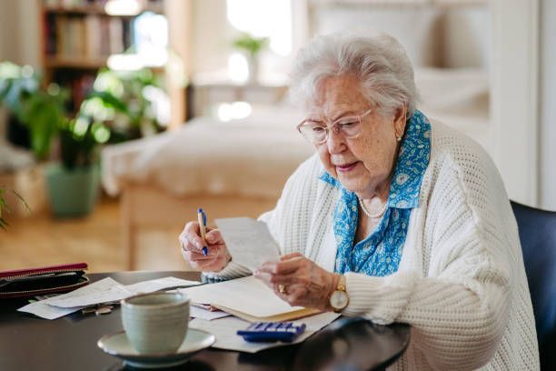 An elderly woman is sitting at a table looking at a piece of paper.