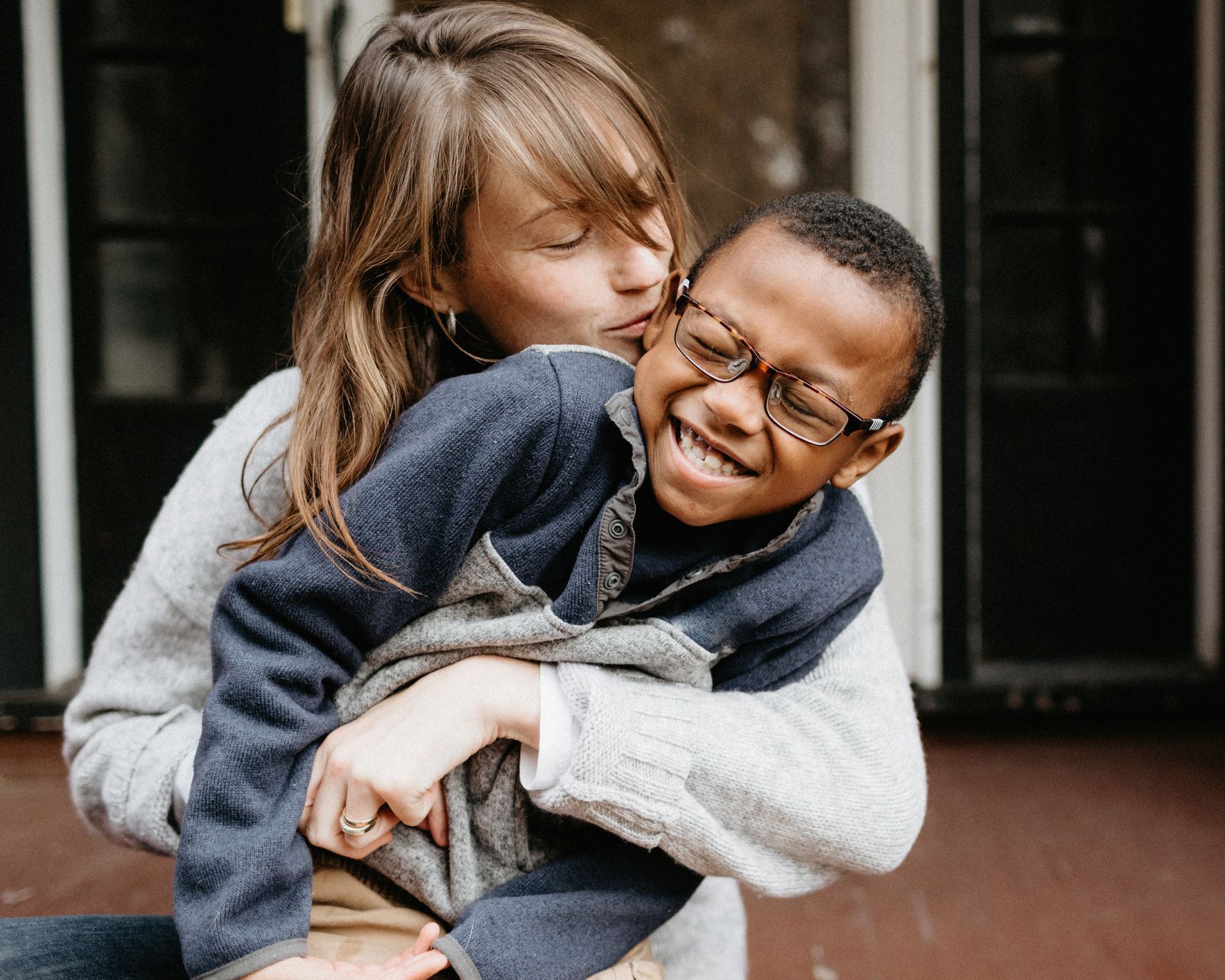 A woman is kissing a boy on the cheek while he is wearing glasses.