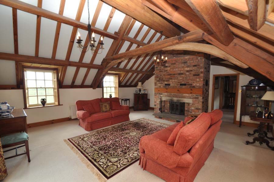 Living room with exposed wooden beams, brick fireplace, red couches, and area rug.