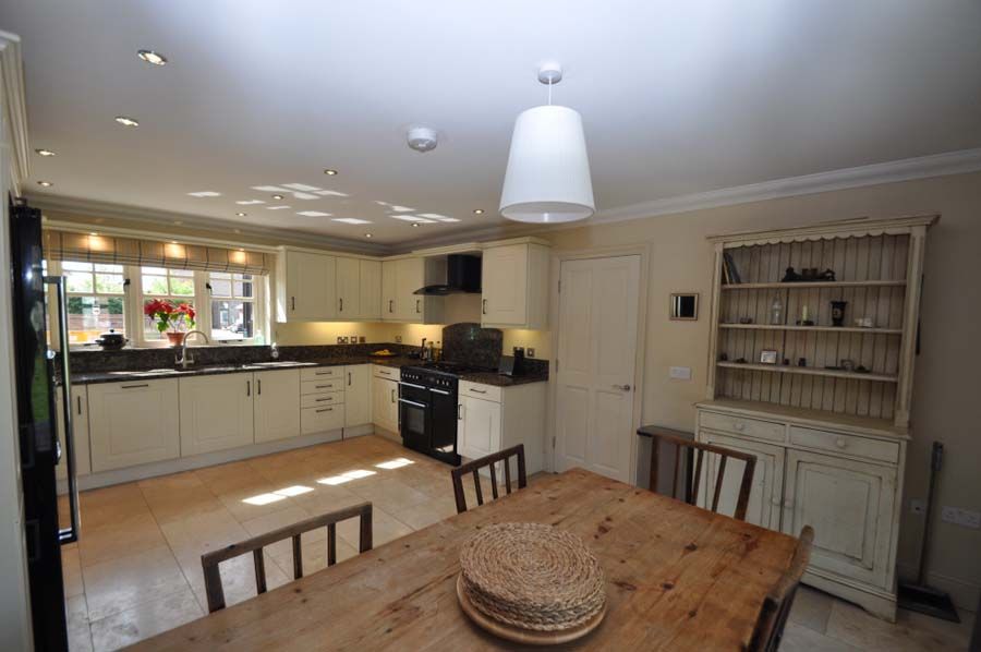 Cream-colored kitchen with wooden table, cream cabinets, and a hutch. Windows to the left, and a pendant light above.