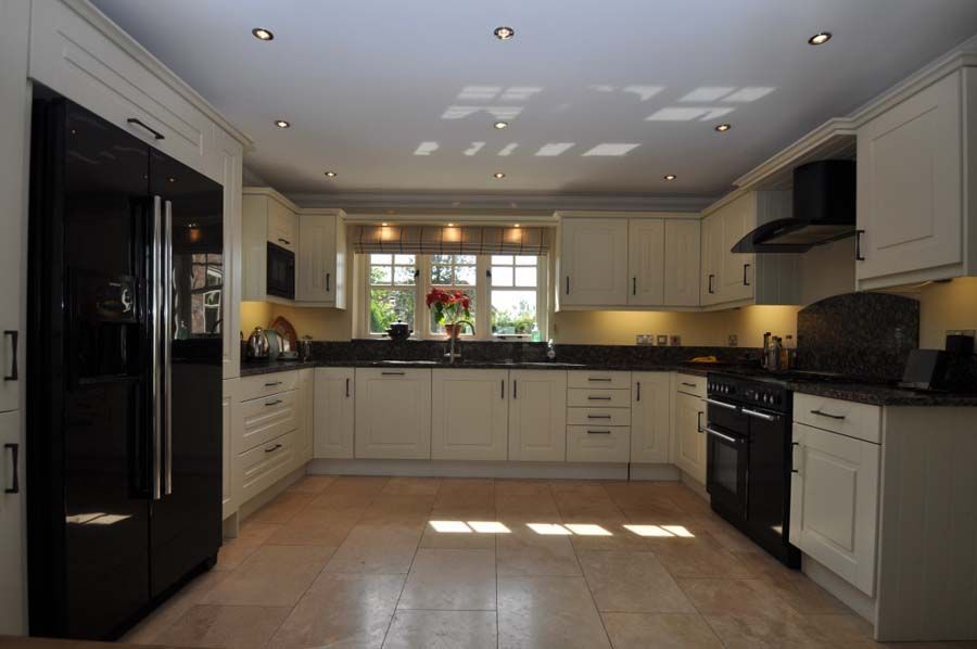 Cream-colored kitchen with black refrigerator and appliances, window with sunlight, beige tile floor.