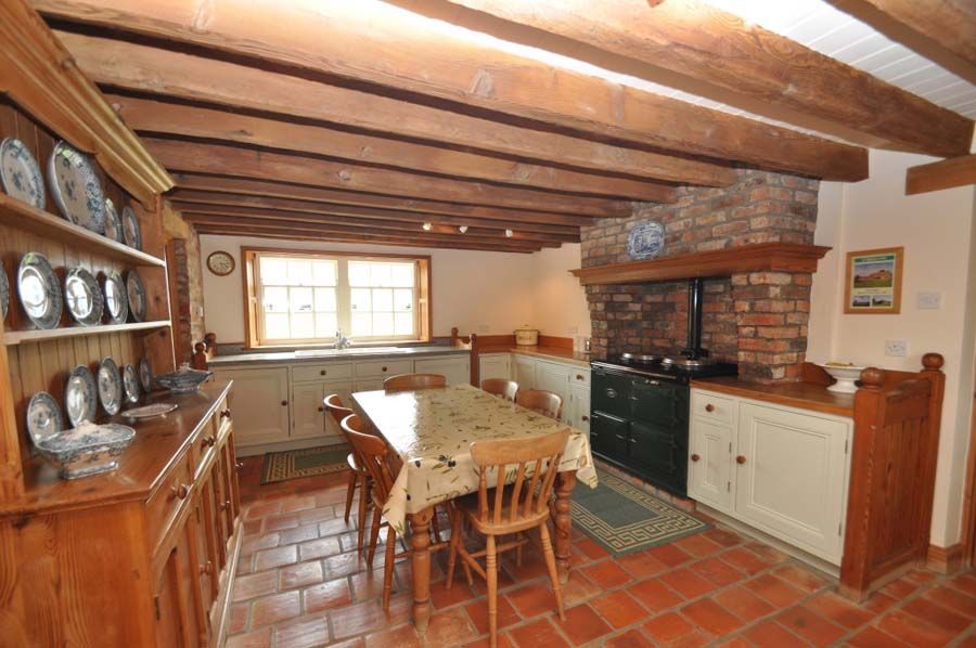 Rustic kitchen with exposed beams, brick fireplace, dining table, and cabinets.