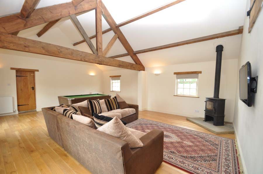 Spacious living room with exposed wooden beams, brown sofas, rug, fireplace, and pool table.