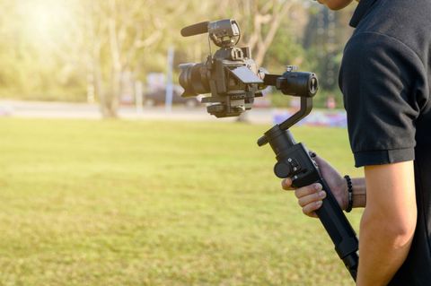 Person holding a camera on a gimbal in a green field, filming outdoors.