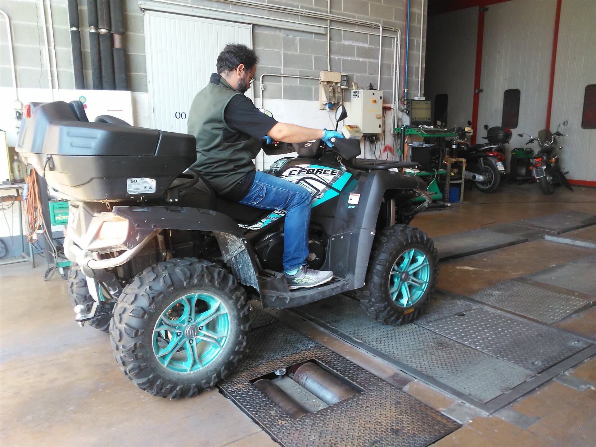 Uomo su un quad verde acqua e nero su un dinamometro in un'officina.